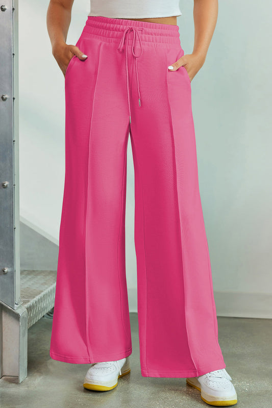 Pink drawstring wide leg pants with pockets and elastic waist, made of polyester, viscose, and elastane blend.